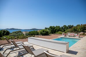 Un espace aménagé au bord de la piscine, avec des chaises longues, une petite piscine et une vue sur la mer.