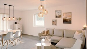 A modern living room with a sofa, dining table, chairs, and pendant lights.