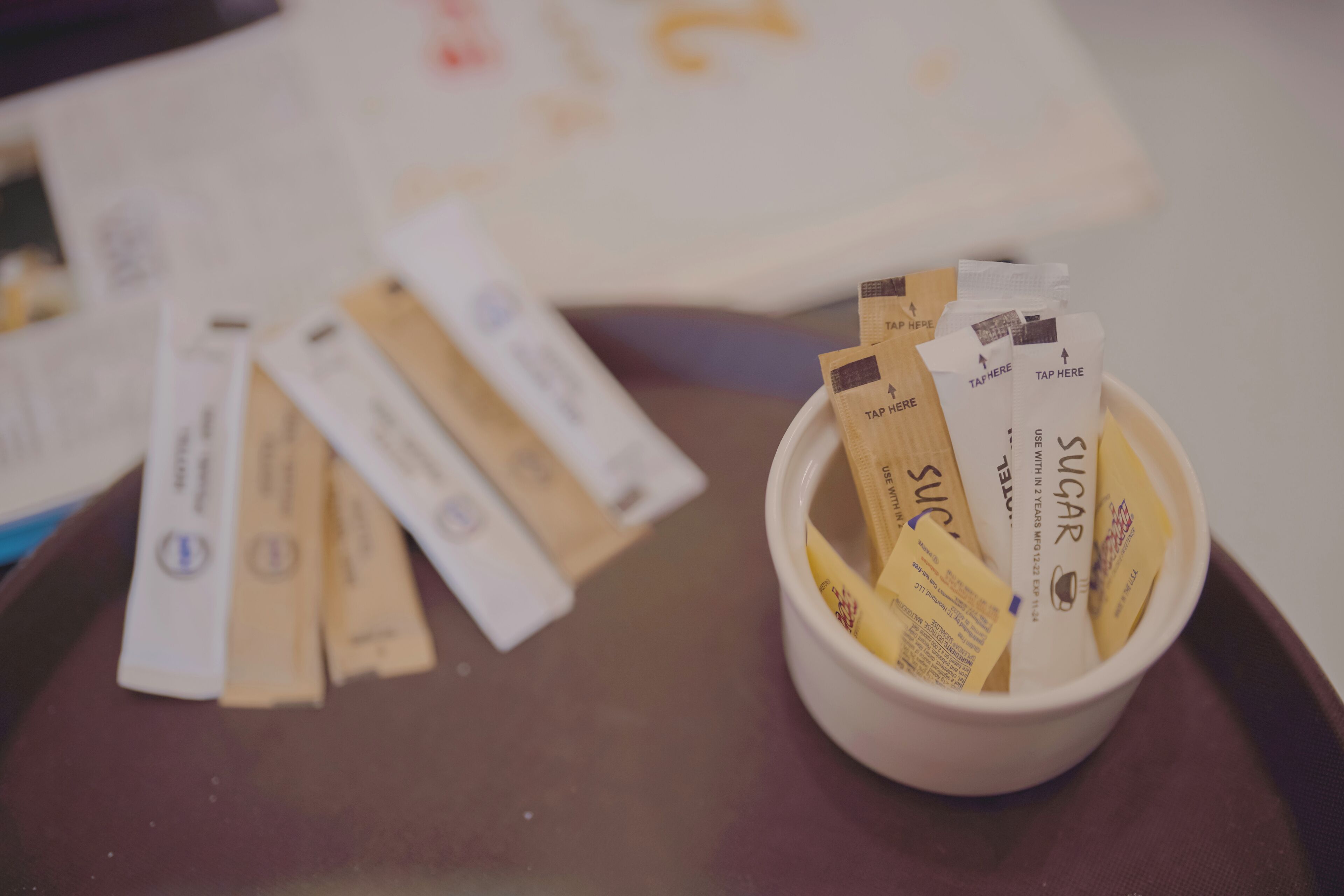 A white bowl filled with sugar packets on a brown tray.