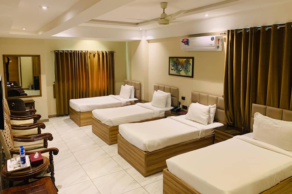 A hotel room with four single beds, a wooden desk with a chair, a mirror, and a ceiling fan.