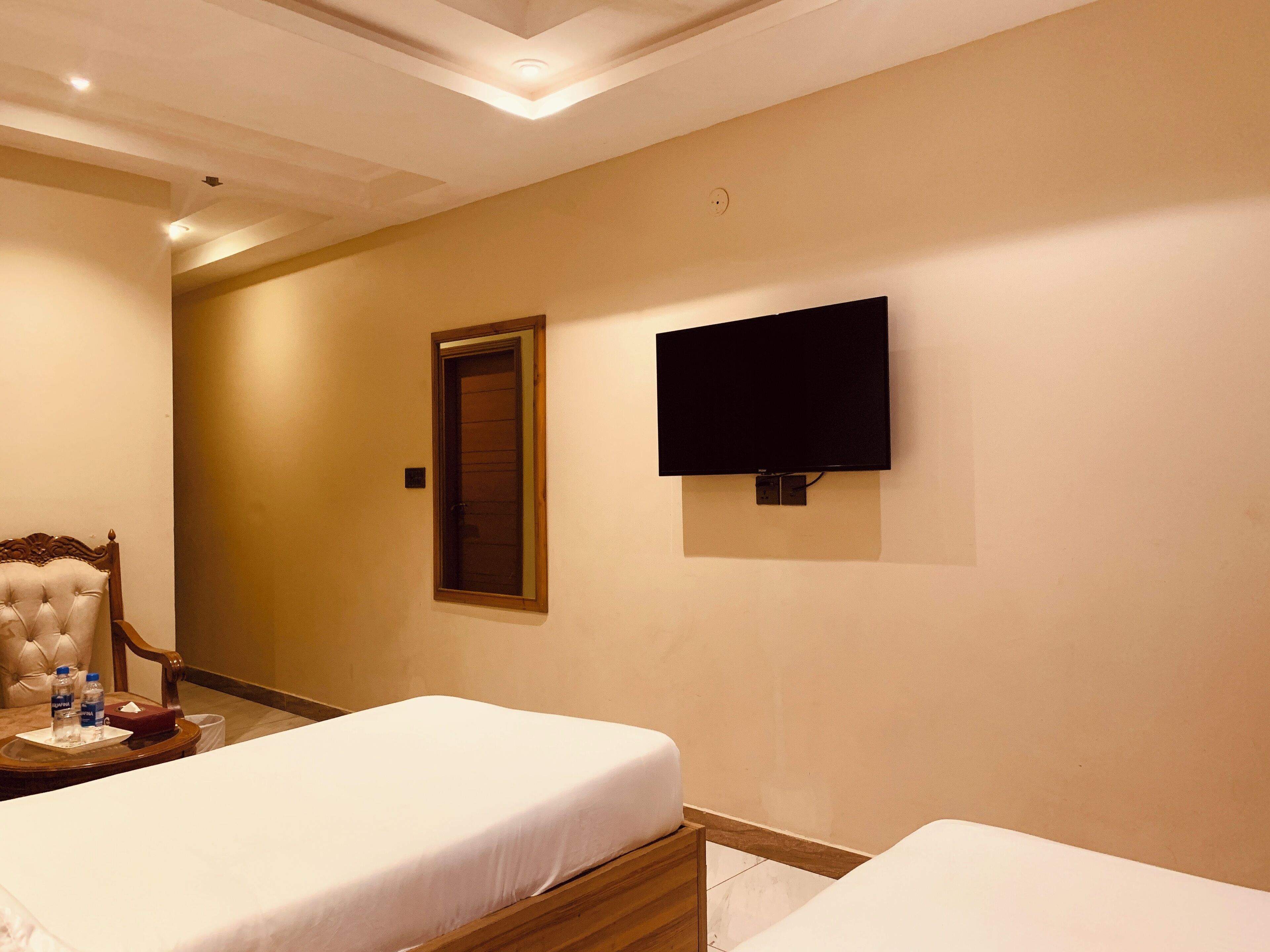 Habitación de hotel con dos camas, un televisor montado en la pared y una puerta al fondo.
