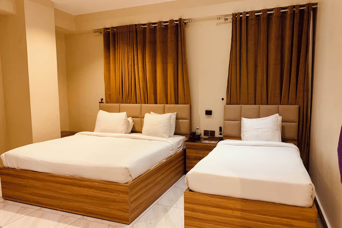 A hotel room with two beds, wooden headboards, beige walls, and curtains.