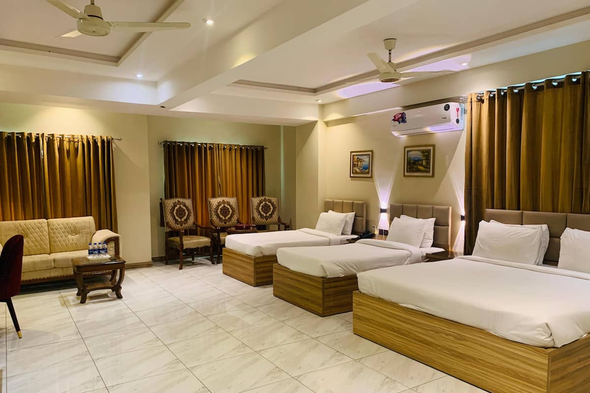 A hotel room with two beds, a sofa, a small table, and a ceiling fan.