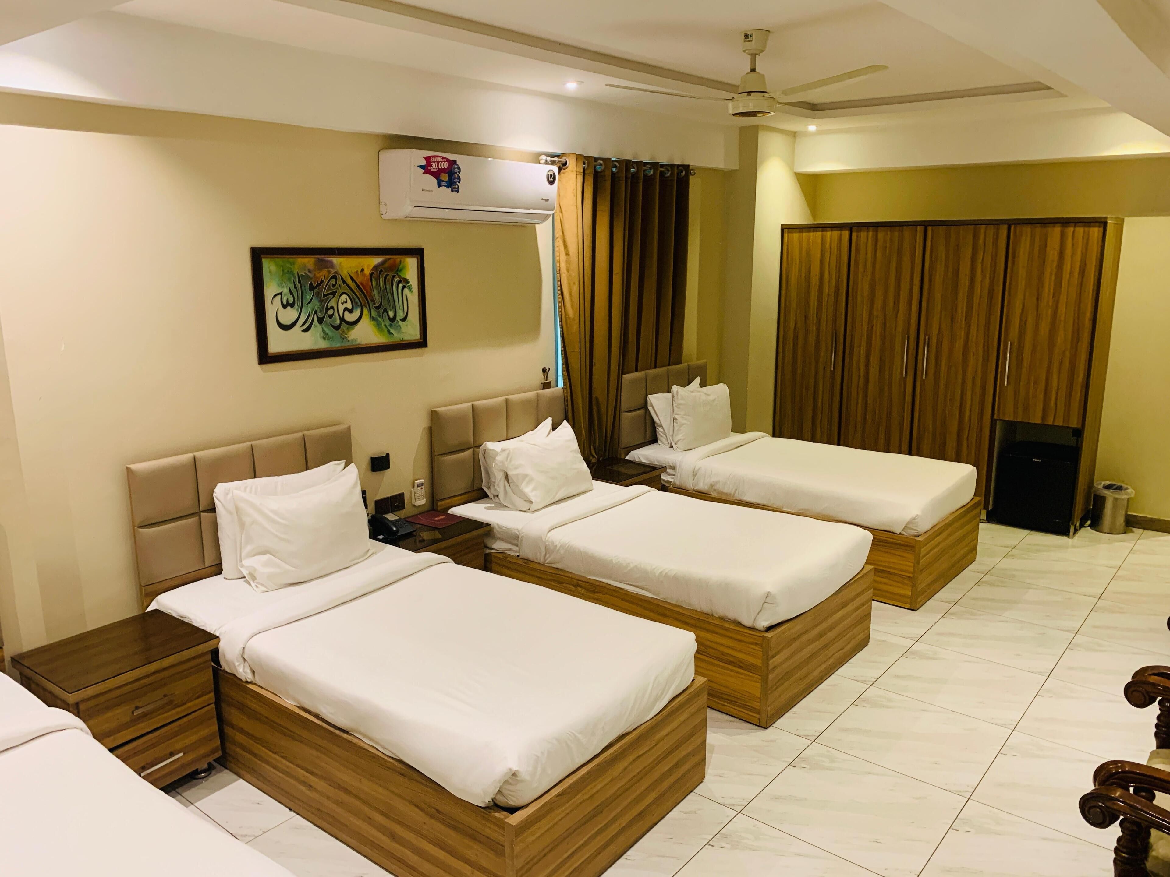 A hotel room with three wooden beds, a ceiling fan, an air conditioning unit, and a painting on the wall.
