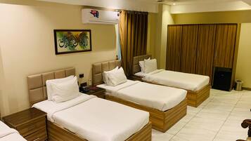 A hotel room with three wooden beds, a ceiling fan, an air conditioning unit, and a painting on the wall.