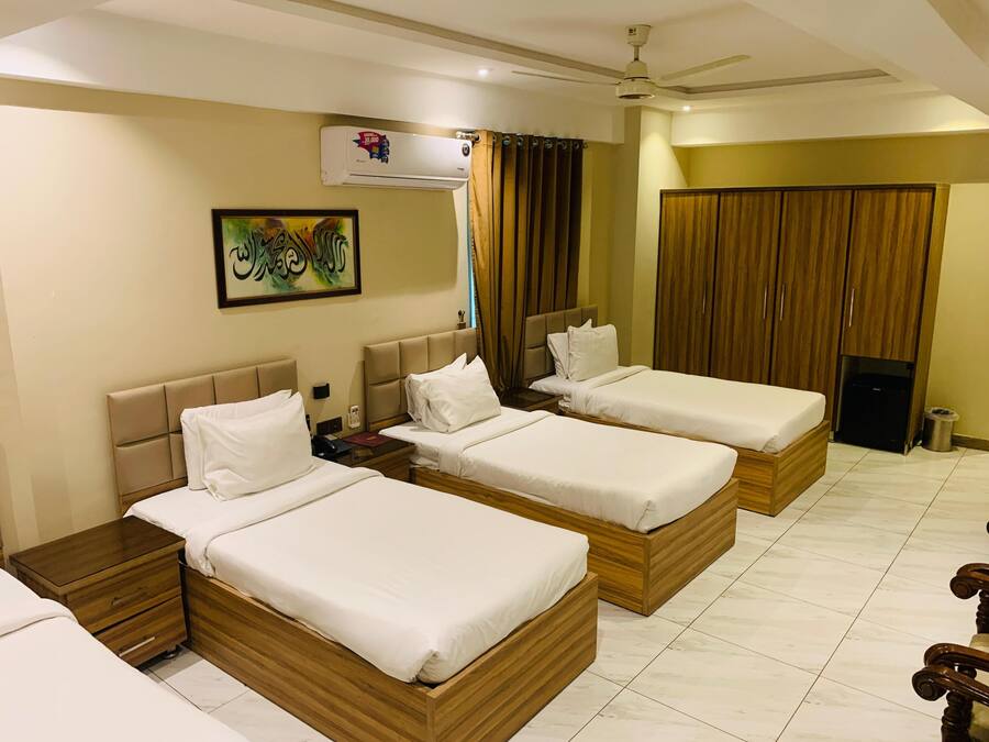 A hotel room with three wooden beds, a ceiling fan, an air conditioning unit, and a painting on the wall.