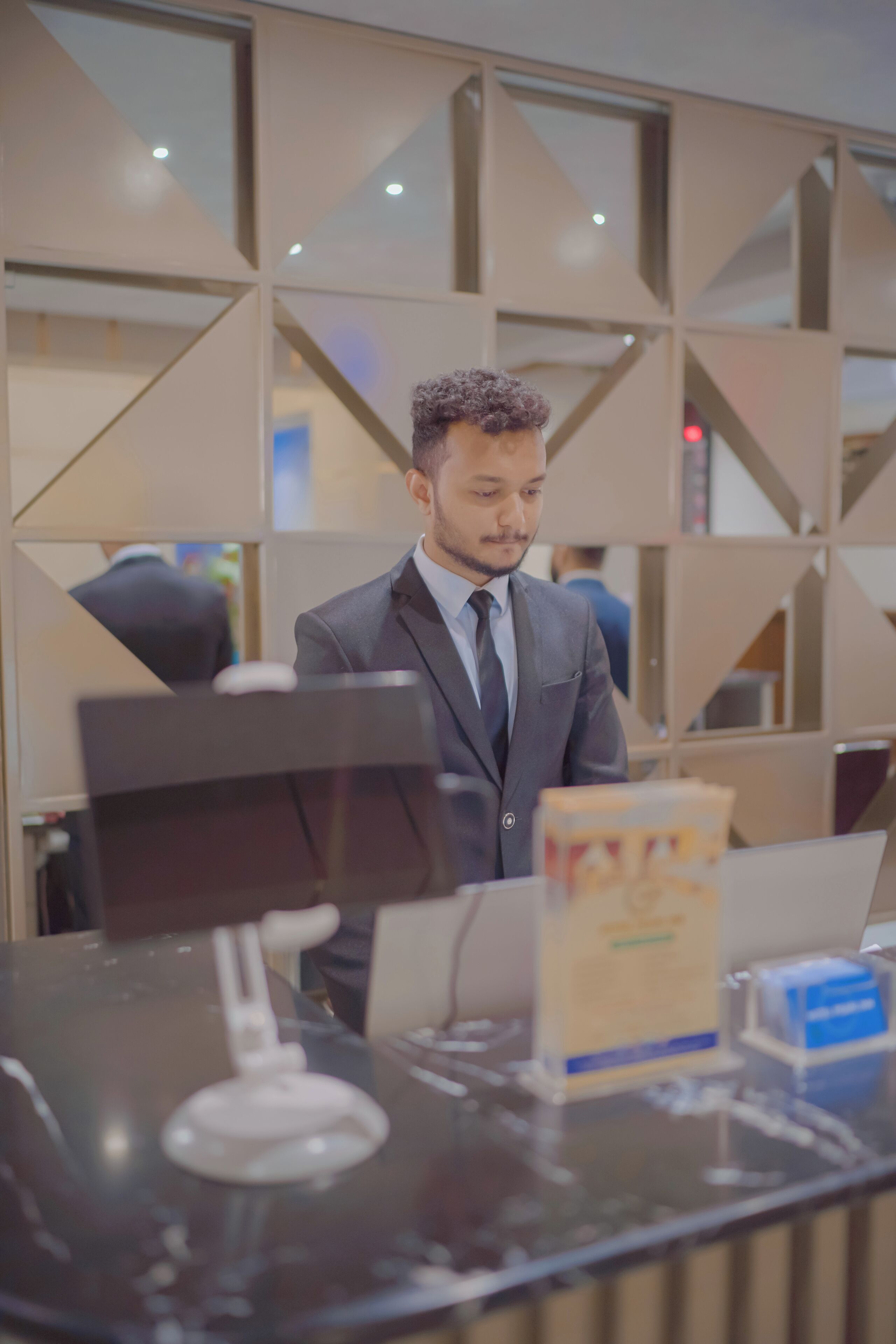 Un homme en costume, derrière un comptoir d’accueil, avec un ordinateur portable, un téléphone et un porte-cartes.