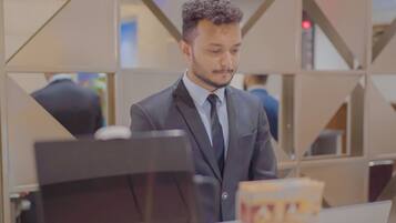 Un hombre con traje en un mostrador de recepción con una computadora portátil, un teléfono y un tarjetero.