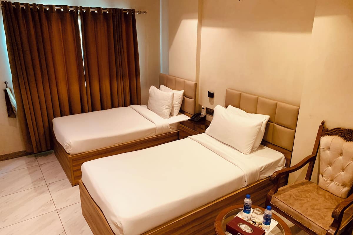 A hotel room with two single beds, a wooden nightstand, a chair, and a small table with a bottle and a box.