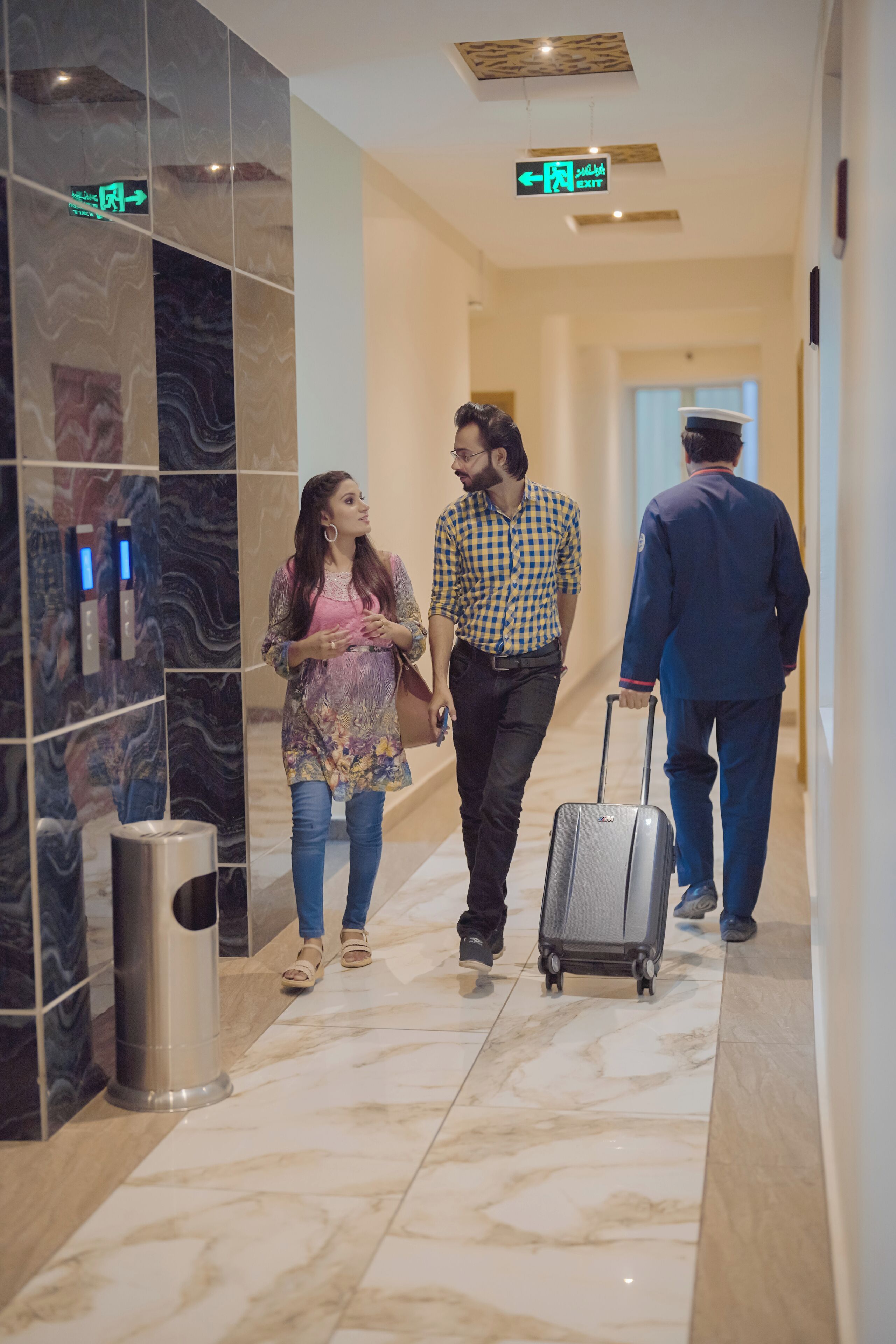 A hotel corridor with marble flooring, a trash bin, and directional signs.