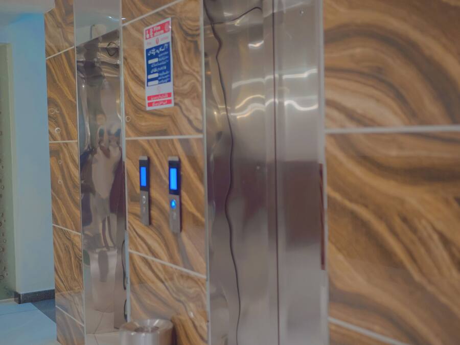 A modern elevator with a wood grain design, a trash bin, and a sign indicating a fire emergency exit.