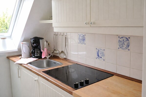 A kitchen with a black induction cooktop, a sink, a coffee maker, and a kettle. There are white cabinets and blue decorative tiles on the wall.