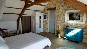 A bedroom with a stone wall, a bed, a blue dresser, and a white door.