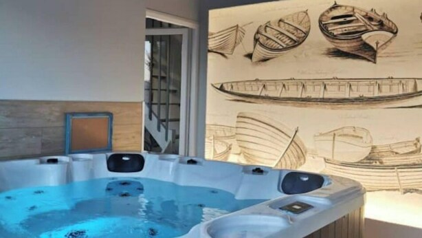 A hot tub with a wooden exterior, surrounded by a room with a large wall mural of boats.