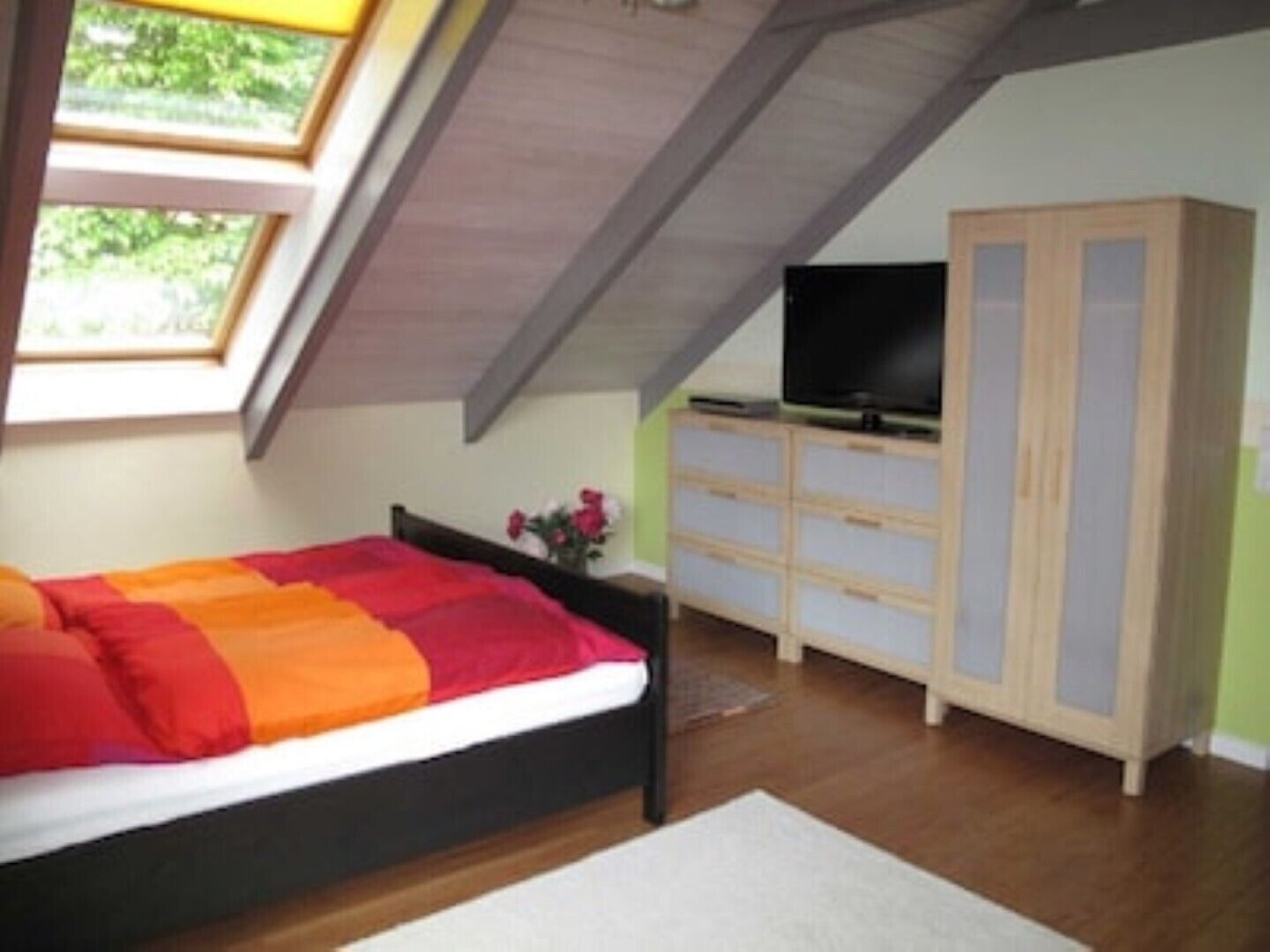Ein Schlafzimmer mit einem Bett, einem Fernseher auf einer Kommode und einem Oberlicht.
