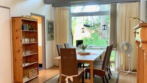 Un comedor con una mesa y sillas de madera, una estantería y un ventanal con cortinas.