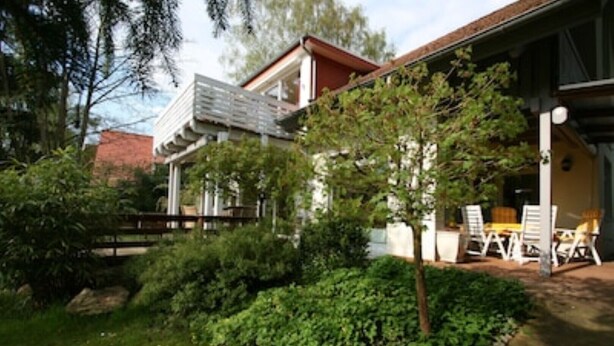 Una casa con porche techado, un pequeño jardín y un área de comedor con mobiliario exterior.