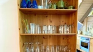 Una estantería de madera con varios objetos, incluyendo libros y cristalería.