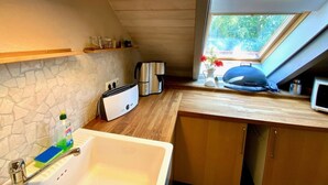 Cocina con protector contra salpicaduras de piedra, horno empotrado, cafetera y ventana con vista a la vegetación.