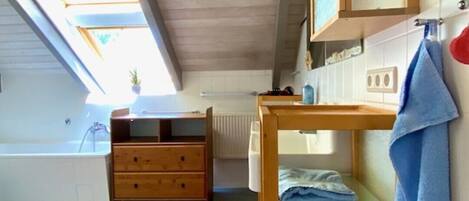 A room with a wooden ceiling, a window with a view, a wooden dresser, a red rug, and a blue towel on a shelf.