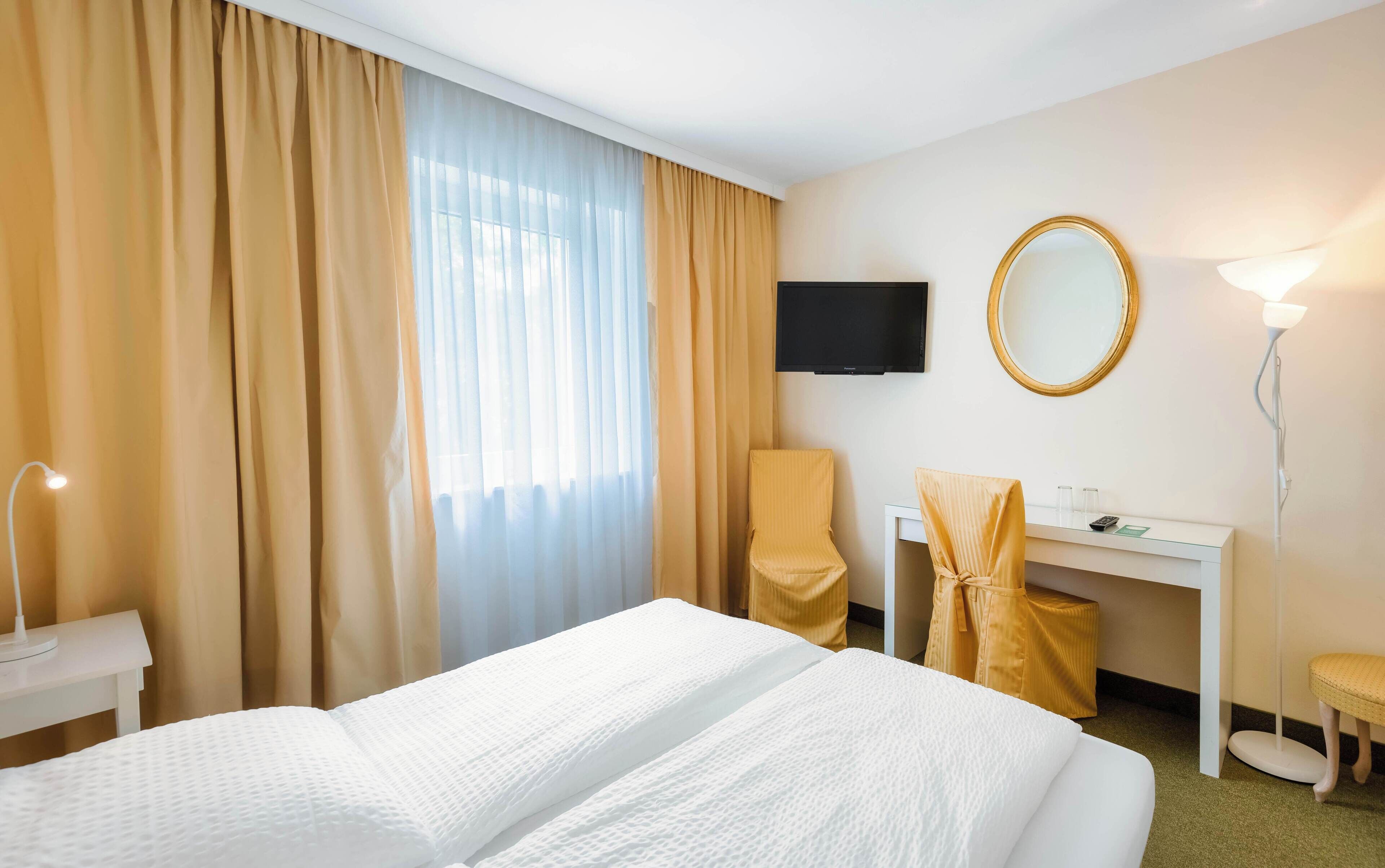 Een hotelkamer met een bed, bureau, stoel, televisie en lamp.