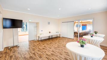 A conference room with a long table, a television, and two round tables with flowers.