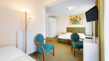 Une chambre d’hôtel avec un lit, deux chaises, un bureau, une télévision et un radiateur.