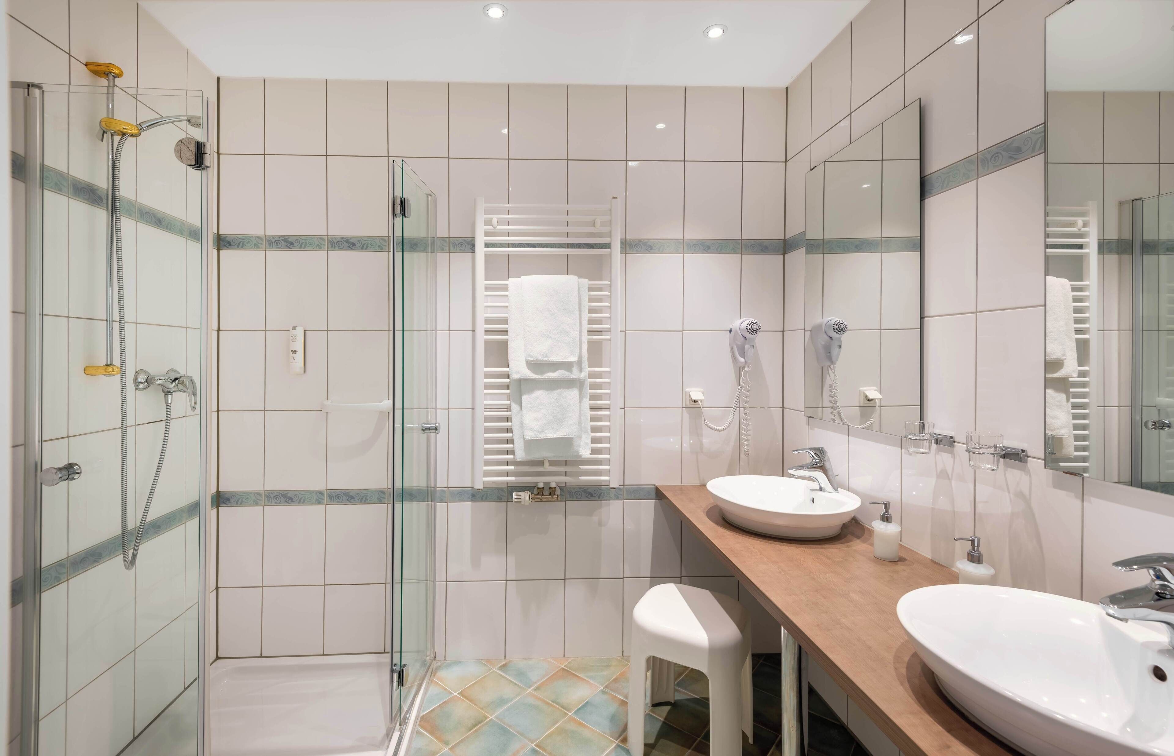 Ein modernes Badezimmer mit einer gläsernen Dusche, zwei Waschbecken, einem Spiegel und einem Handtuchhalter.