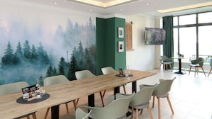 Ein Essbereich mit einem langen Holztisch, mehreren Stühlen, einer Wandmalerei eines Waldes und einem Fernseher an der Wand.