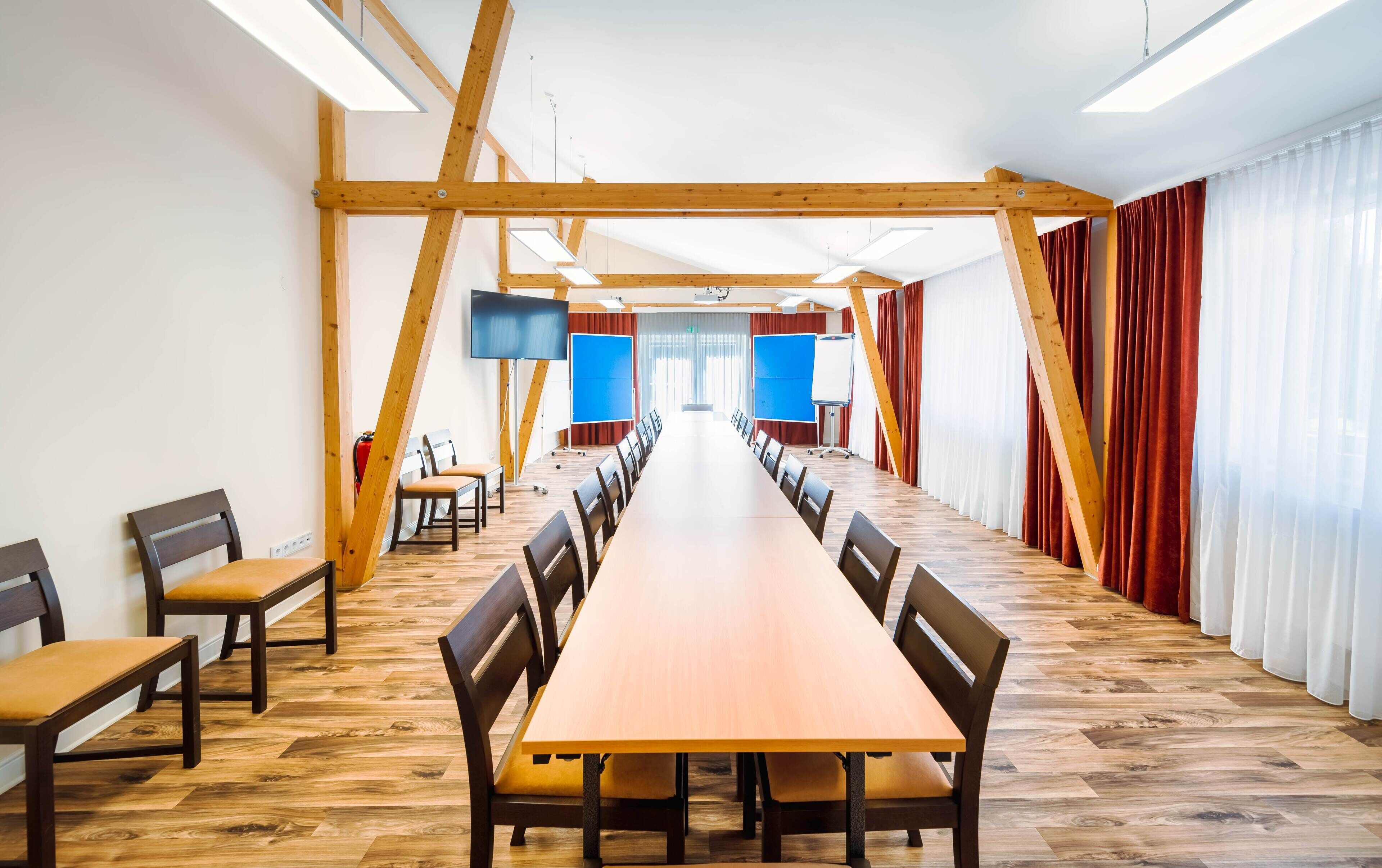 Un salón de conferencias con una larga mesa de madera, múltiples sillas, un televisor de pantalla plana grande y una pizarra.