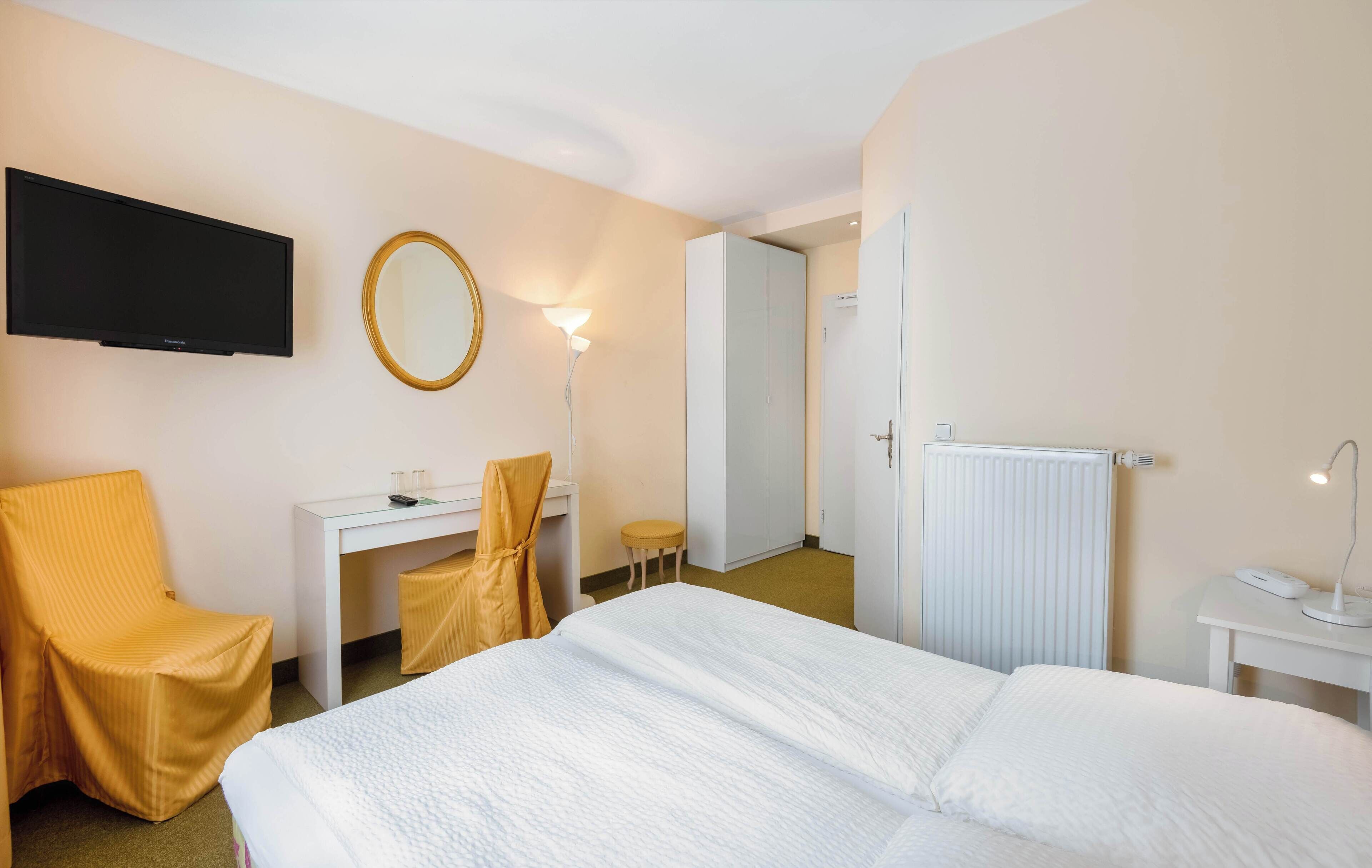 A hotel room with a bed, a desk, a chair, a TV, a mirror, and a lamp.