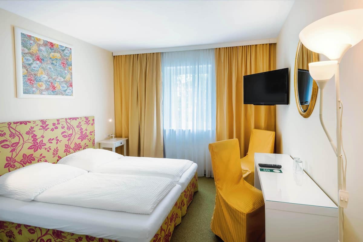 Una habitación de hotel con cama, escritorio, silla, televisor y un cuadro en la pared.