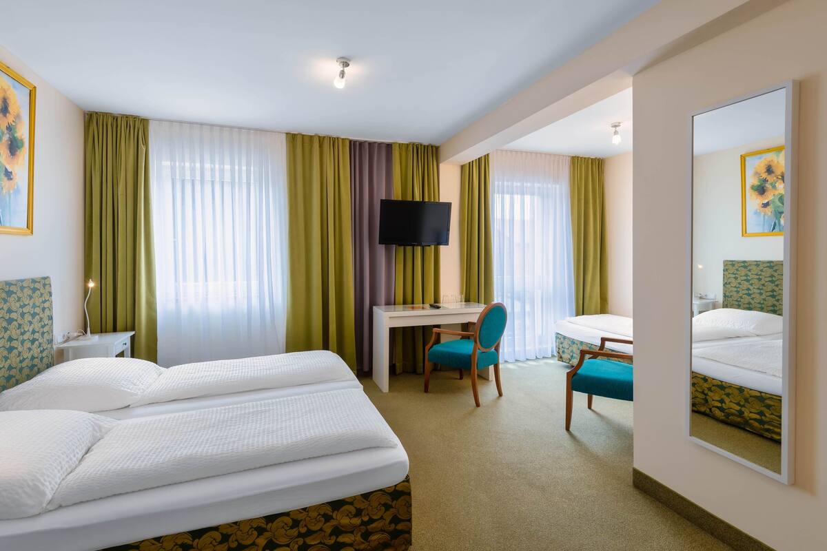 Habitación de hotel con dos camas, un escritorio, una silla, un televisor y un espejo grande.