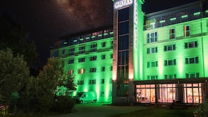 Ein Hotel mit einem großen 'HOTEL'-Schild an der Ecke, mehreren Etagen und einem Parkplatz, auf dem ein Lieferwagen steht.