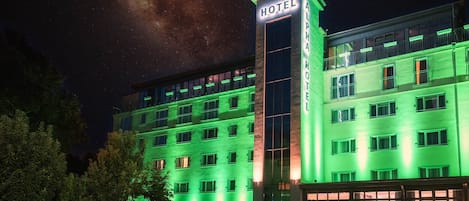 A hotel with a prominent 'HOTEL' sign on the corner, multiple floors, and a parking area with a van.