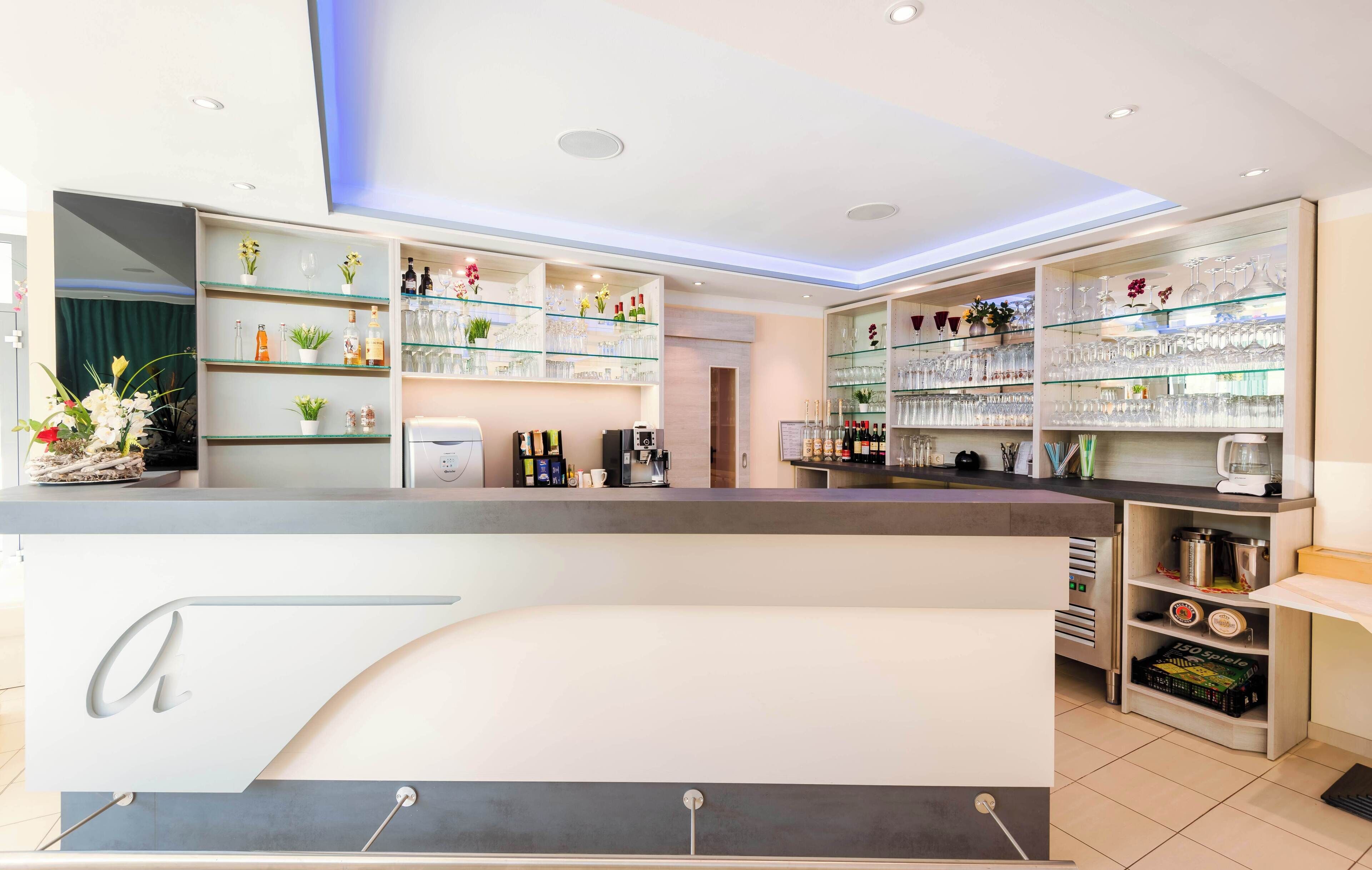 Zona de bar moderna con estantes de vidrio que exhiben botellas y vasos, una máquina de café y una barra con una placa de identificación.