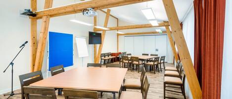 A conference room with a large table, multiple chairs, wooden beams, a projector, and a television.