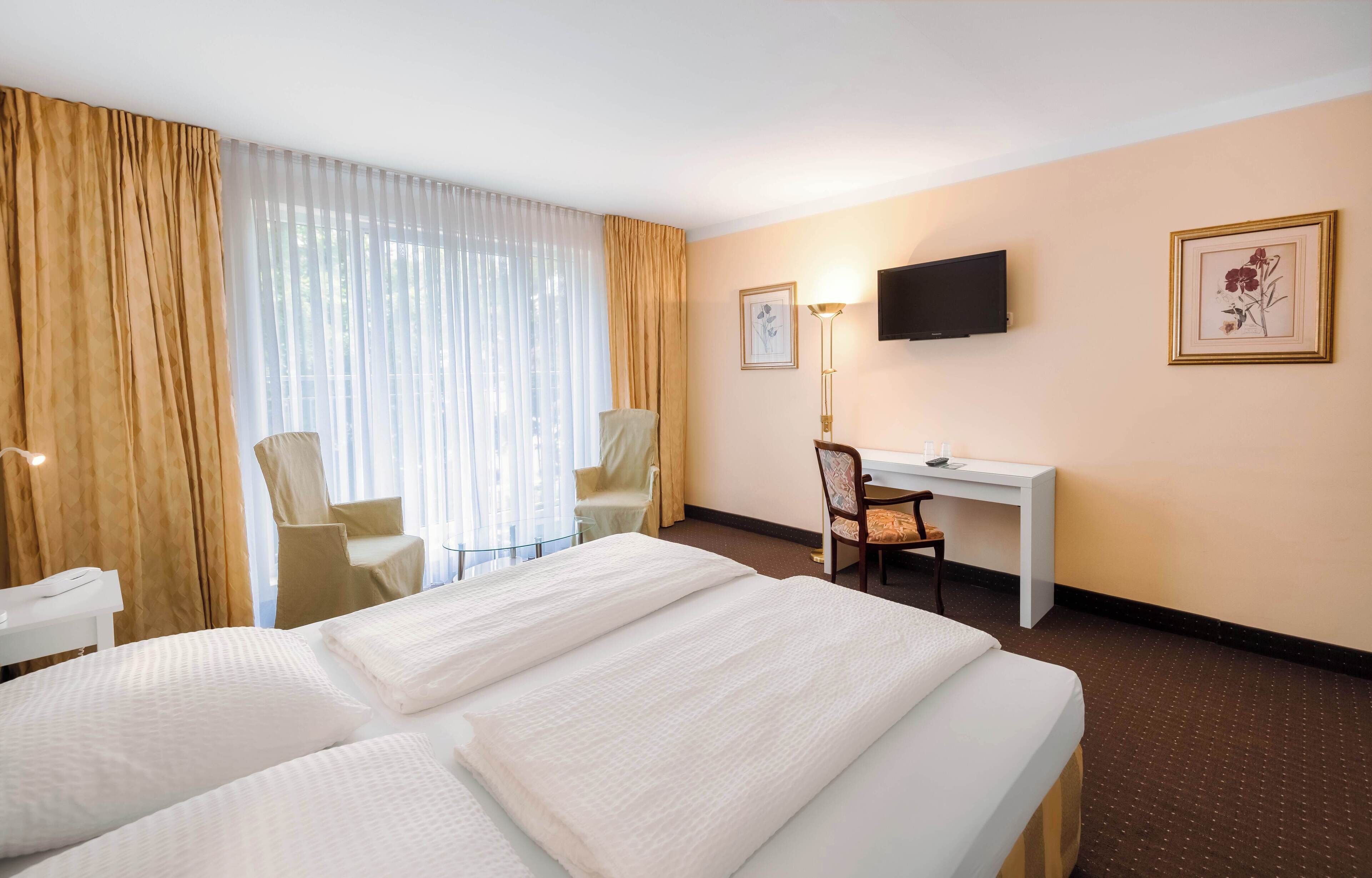 Une chambre d’hôtel avec deux lits, un bureau, une chaise, une télévision et un tableau encadré au mur.