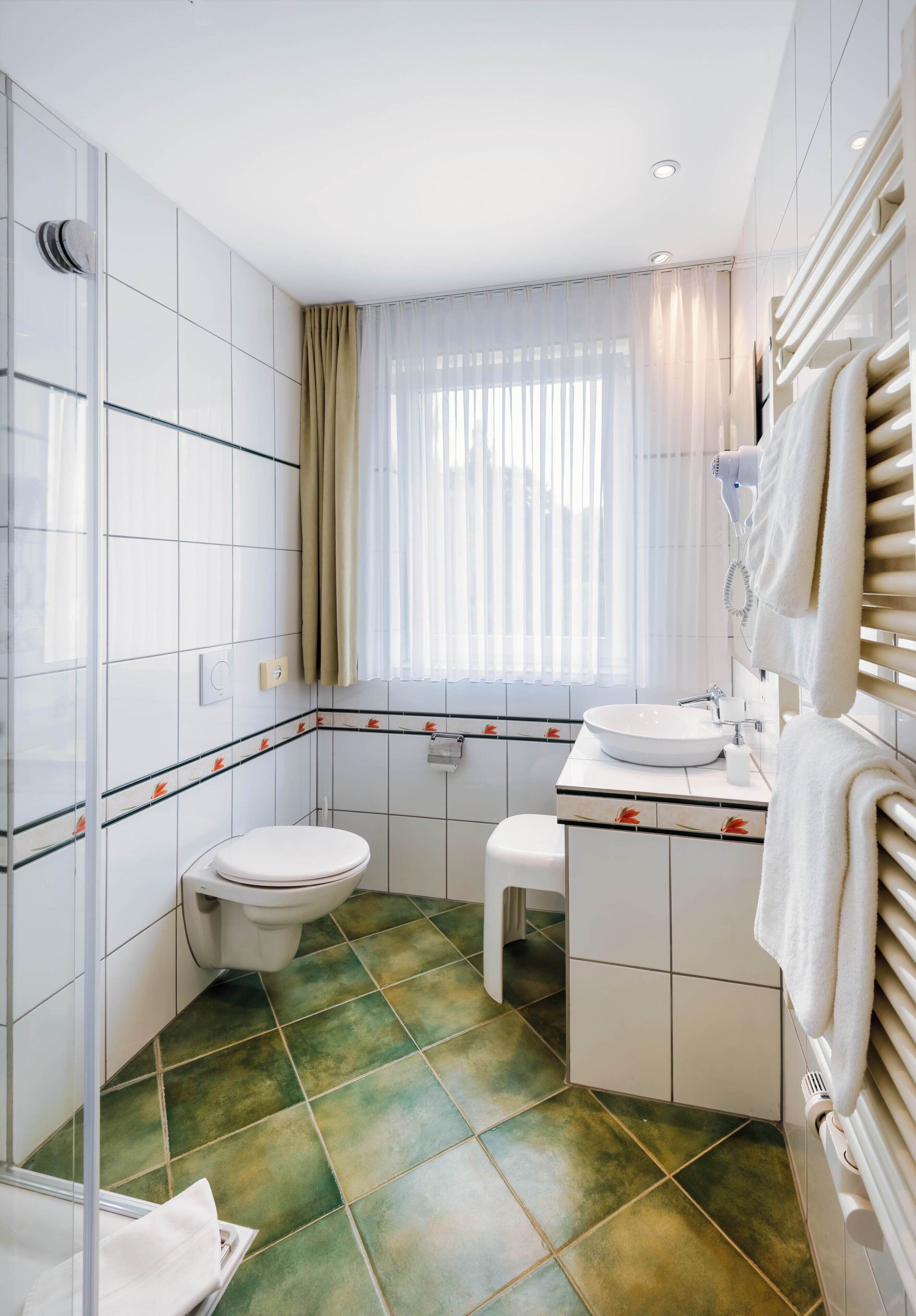 A bathroom with a toilet, sink, and mirror. There is a window with curtains and a towel rack.