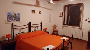 A bedroom with a bed, a nightstand, a chair, a window, and a ceiling fan. - Letizia apartment in farmhouse in the countryside (Bivio Ravi)