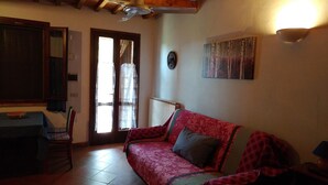 A living room with a red sofa, a wooden ceiling, a wall-mounted clock, and a painting. - Letizia apartment in farmhouse in the countryside (Bivio Ravi)