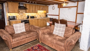 A cozy kitchen with wooden cabinets, a microwave, and a coffee maker. There are two brown sofas with plaid pillows and a red patterned rug. - The Coach House 4 bed, 4 bathroom cottage (Porthcawl)