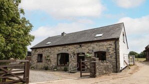 A stone building with a sloped roof, a wooden gate, and a gravel driveway. - The Coach House 4 bed, 4 bathroom cottage (Porthcawl)