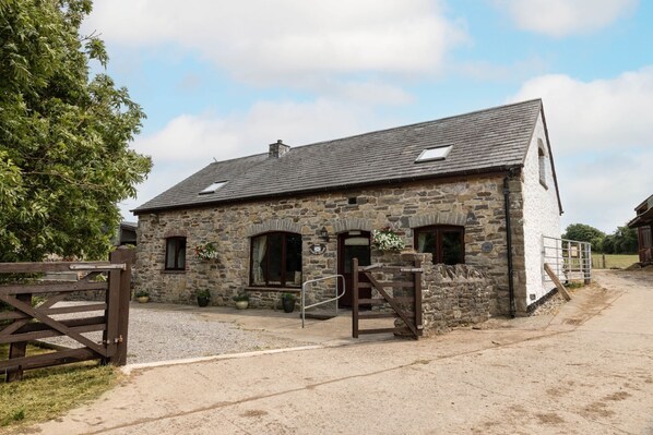 A stone building with a sloped roof, a wooden gate, and a gravel driveway. - The Coach House  4 bed, 4 bathroom cottage (Porthcawl)