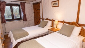 A room with two single beds, wooden headboards, a nightstand with a lamp, a radiator, and a window with curtains. - The Coach House 4 bed, 4 bathroom cottage (Porthcawl)