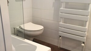A bathroom with a white toilet, a glass-enclosed bathtub, and a white towel rack. - Cozy Studio for 4 in Heart of Alpe d'Huez, South-Facing Terrace, Pet-Friendly (Huez)