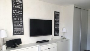 A modern living room with a flat-screen TV mounted on the wall, a white console table with a lamp, and two framed motivational posters. - Cozy Studio for 4 in Heart of Alpe d'Huez, South-Facing Terrace, Pet-Friendly (Huez)