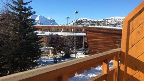 A wooden balcony overlooking a snowy mountain landscape with a building in the background. - Cozy Studio for 4 in Heart of Alpe d'Huez, South-Facing Terrace, Pet-Friendly (Huez)