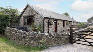 A stone cottage with a sloped roof, a wooden gate, and a stone wall.