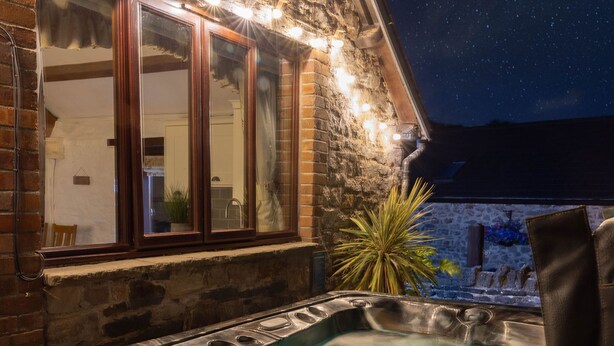 A hot tub in front of a stone building with a starry night sky visible through the window.